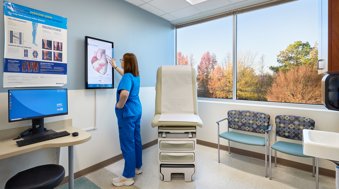 A provider uses the tablet that is mounted on the wall inside the exam room