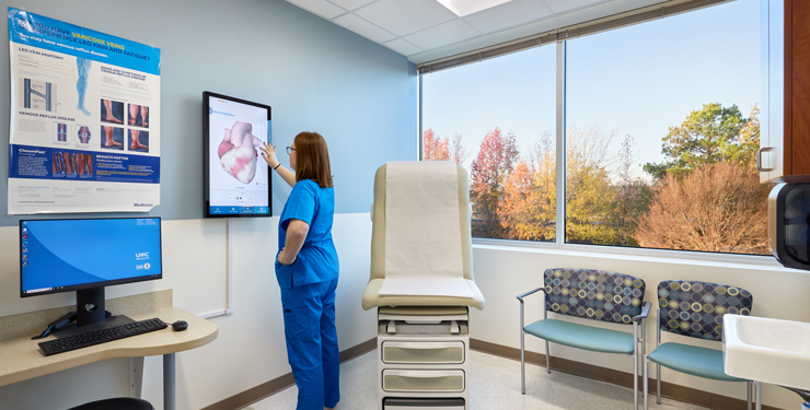 A provider uses the tablet that is mounted on the wall inside the exam room