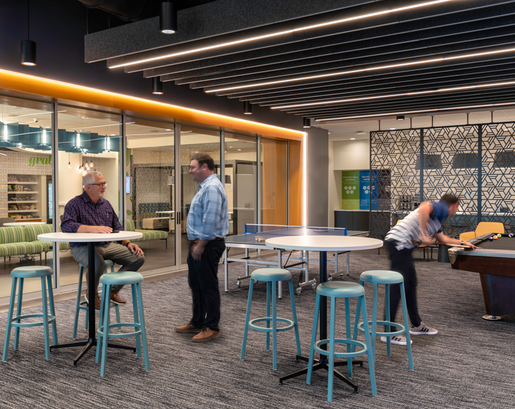 Employees talk at a high top table while another plays pool