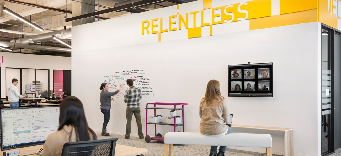 Virtual team members are shown on a monitor in the office