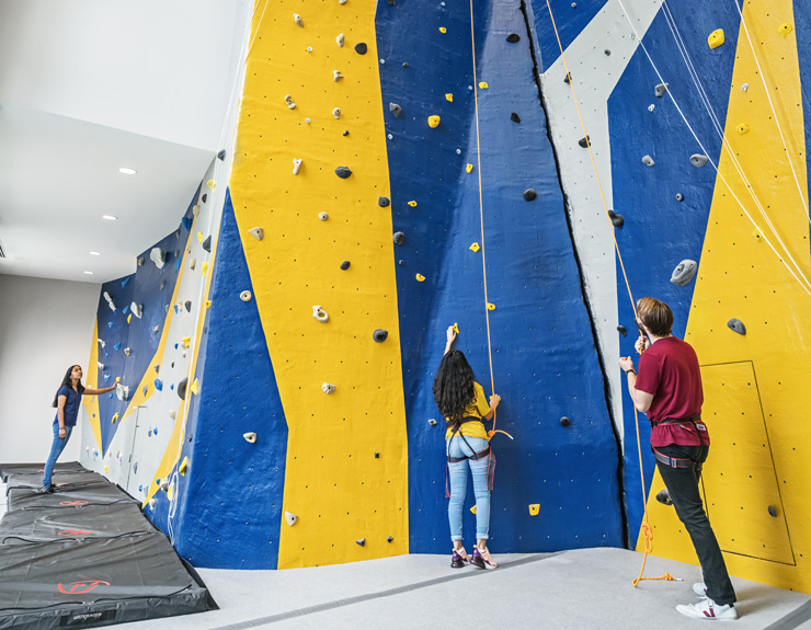 Two students stand at the bottom of the rock-climbing wall