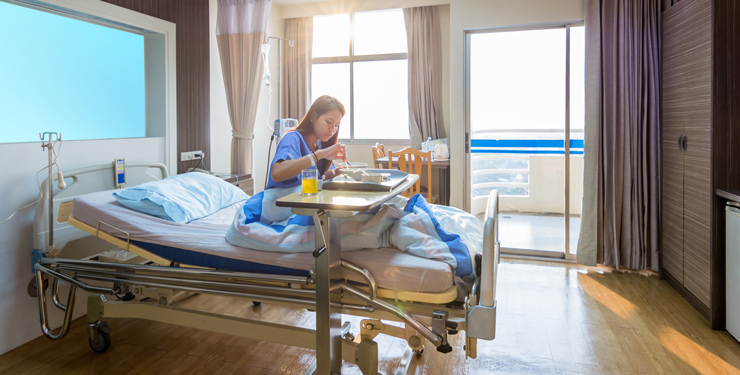 A patient sits in their bed eating off a tray of food